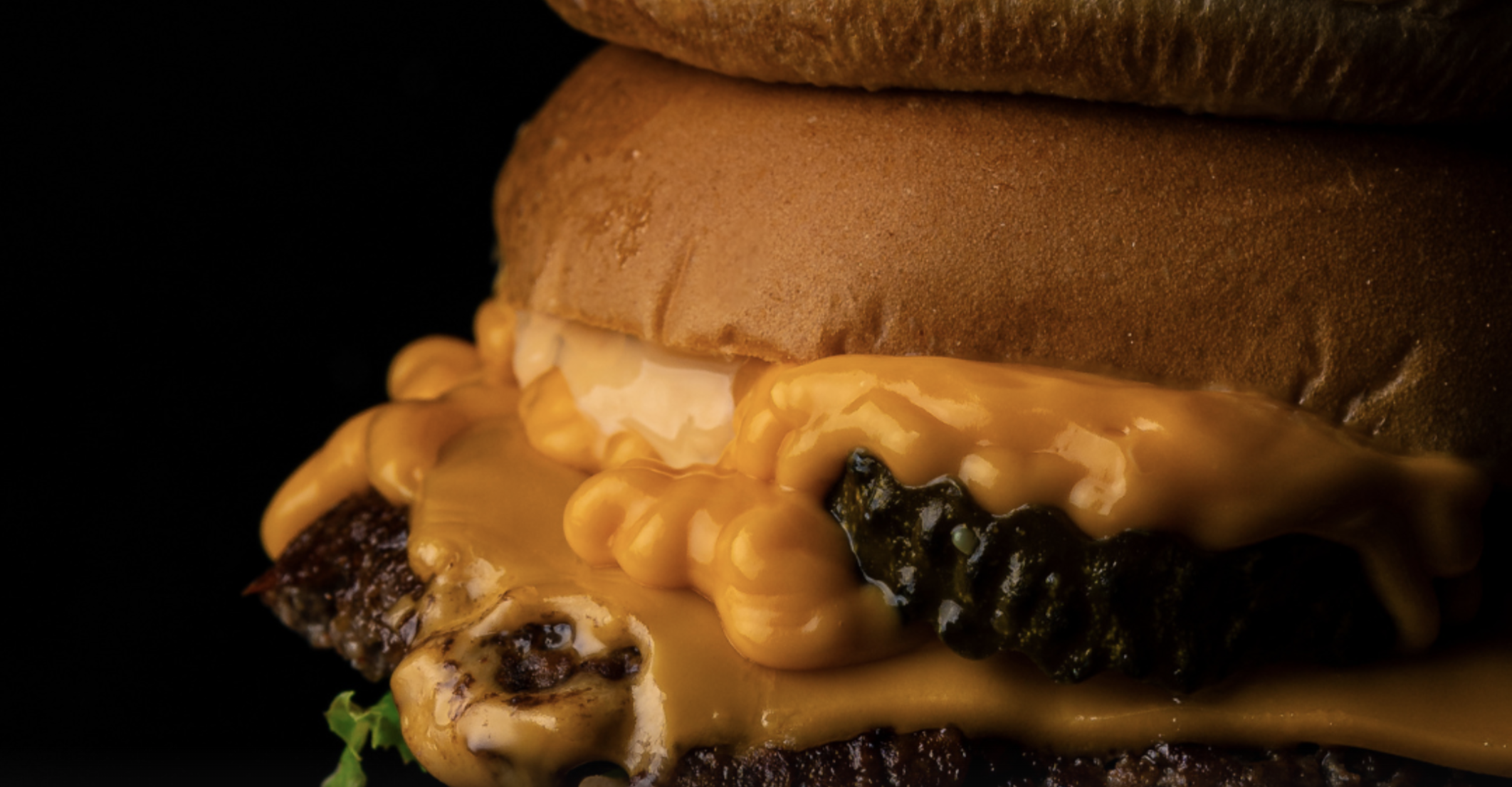 a close up of our signature burger with beef, cheese and a gerkin peeking out of the side.